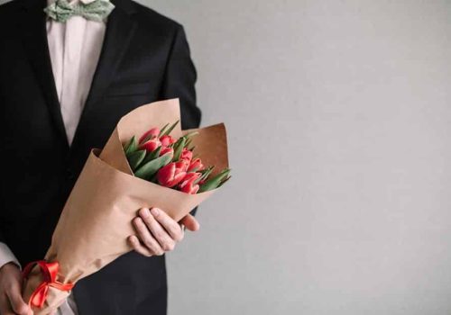 Handsome man in an elegant suit giving a bouquet of yellow tulips. Valentine's Day, Women's Day, Mother's Day. Wedding concept. Copy space.