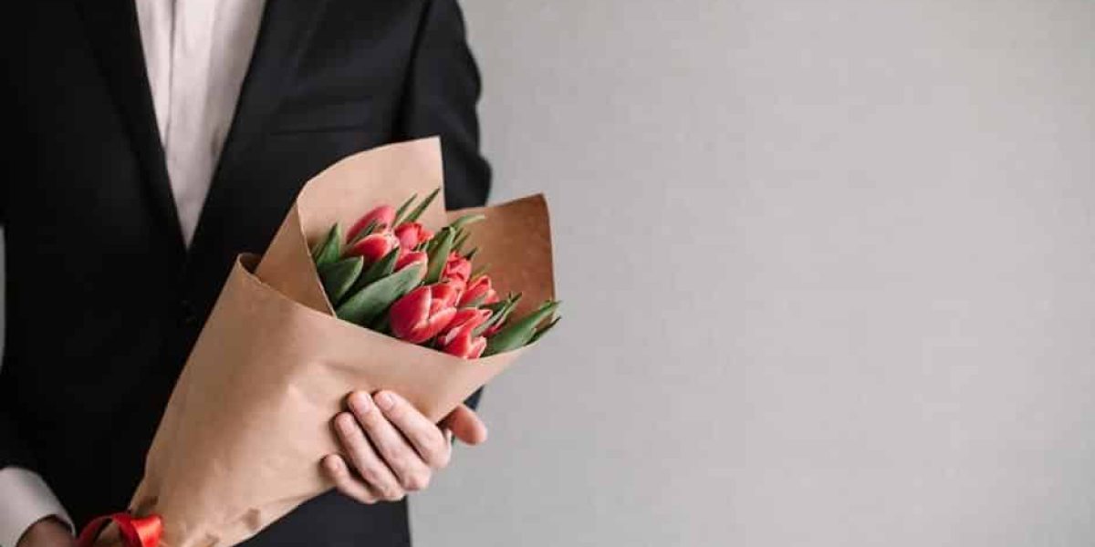 Handsome man in an elegant suit giving a bouquet of yellow tulips. Valentine's Day, Women's Day, Mother's Day. Wedding concept. Copy space.